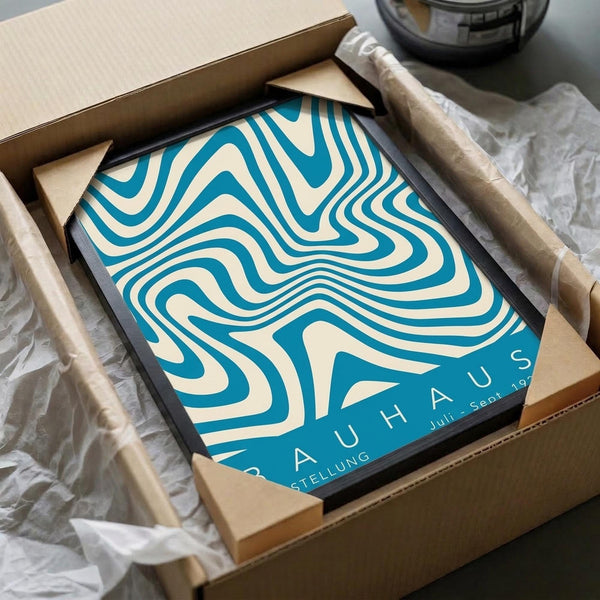 May include: Framed blue and cream abstract poster with flowing, wavy contour lines in Bauhaus style, packaged in brown cardboard box with protective tissue paper wrapping, photographed on white fabric surface next to glass object.