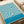 May include: Vintage-style poster with flowing turquoise and cream wave pattern displayed on light wood surface next to beige couch. Design features organic curved lines creating topographical effect with "BAUHAUS AUSSTELLUNG Juli-Sept 1923" text in modern typography at bottom right corner.