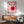 May include: Pink Bauhaus poster with red circles and white geometric shapes in wooden frame, displayed above mid-century modern wooden credenza with white ceramic table lamp. Mint green upholstered armchair with wooden arms sits nearby on hardwood floor. Natural sunlight creates dramatic shadows on white wall in minimalist living room setting.