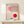May include: A framed Bauhaus-style poster with geometric pink and red circular shapes intersected by curved parallel lines, displayed on a light wood console table beside a small wrapped gift with twine and evergreen sprig. The minimalist artwork features a cream background with the word "BAUHAUS" at the top, presented in a natural wood frame against a white wall.