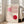 May include: Framed Bauhaus-style poster with geometric design featuring pink and red circles intersecting with curved linear patterns on cream background, displayed against white wall next to beige upholstered chair in bright living room with large windows and natural lighting