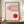 May include: Framed Bauhaus exhibition poster in modern minimalist style featuring geometric red and pink circular forms with curved linear patterns on cream background, displayed on wooden console beside white ceramic vase and books in elegant room with cream walls and architectural molding.