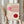 May include: Person holding framed Bauhaus exhibition poster with geometric design featuring pink and red curved lines and circles on cream background. Dried pampas grass visible to left. Neutral home interior with beige clothing and soft lighting.