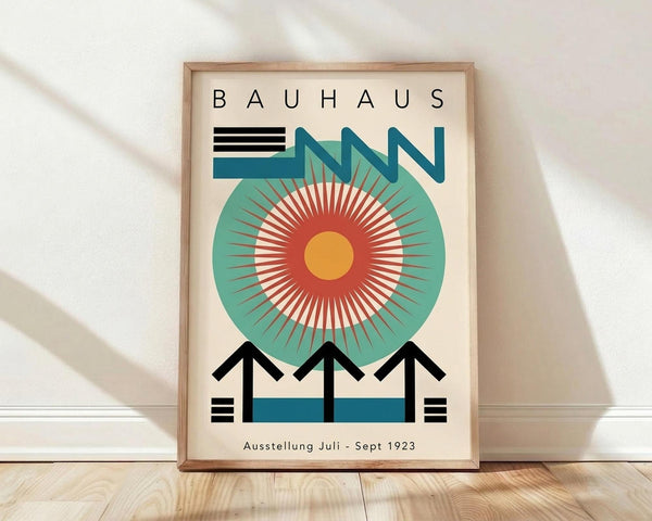May include: Framed Bauhaus-style poster with geometric design featuring a large teal circle with radiating red and white rays around yellow center, black horizontal lines and angular shapes, displayed against white wall on light wooden floor with soft shadows