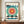 May include: Framed Bauhaus-style poster with geometric design featuring a large circular sunburst in coral, yellow and teal colors, black angular shapes, and "BAUHAUS" text at top. The cream-colored print is displayed in a brown wooden frame on a mid-century modern wooden sideboard next to a white ceramic vase and stack of books in a minimalist room setting.