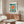 May include: Vintage Bauhaus exhibition poster with geometric design featuring large teal circle, radiating orange and red sunburst pattern, black angular shapes, and "BAUHAUS" text at top. Displayed in thin brown frame above walnut credenza in modern living room with cream curved chair, glass oval coffee table, and white table lamp.
