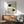May include: Framed Bauhaus exhibition poster with geometric design featuring black and green circles connected by curved linear patterns on cream background, displayed above mid-century modern wood credenza with ceramic lamp, next to sage green upholstered armchair with wooden arms in sunlit room with white walls