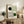 May include: Framed Bauhaus-style poster with geometric design featuring black and green circles intersected by curved linear patterns, displayed on rustic wooden sideboard alongside fern plant, ceramic vase, and leather armchair in modern neutral-toned living room setting.
