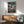 May include: Framed One Piece anime poster featuring Luffy in red shirt and straw hat leaping from a wooden boat against stormy ocean backdrop with dramatic clouds. The vintage-style artwork shows Japanese text and "Journey Beyond the Horizon" subtitle. Displayed above mid-century modern walnut credenza with white ceramic lamp, next to sage green upholstered armchair with wooden frame in bright, naturally-lit room with white walls.