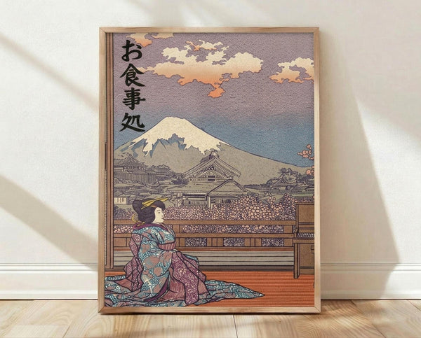 May include: A framed Japanese woodblock print artwork leaning against a white wall on light wooden flooring. The print features a geisha in colorful robes sitting on a wooden platform, gazing toward snow-capped Mount Fuji in the distance. Traditional architecture and cherry blossoms fill the middle ground under a dusky sky with warm clouds. Japanese characters appear in the upper left corner. The piece has muted earth tones with pops of pink and blue, displayed in a simple wooden frame.