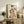 May include: Framed vintage Japanese artwork featuring a geisha in colorful floral kimono holding a decorative fan, displayed on weathered wood sideboard with aged patina background, surrounded by fern plant, ceramic vase, and books in neutral-toned living room setting