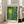 May include: Framed art print leaning against white wall next to beige sofa in bright room with large windows. Print features abstract design with bright yellow sun, teal and green vertical stripes, scattered dots, and dark foliage silhouettes. Text reads "YAYOI KUSAMA" at top, "Modern Art" and "1964" at bottom. Light wood frame, cream matting.