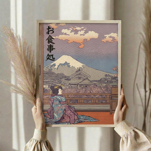 May include: Hands holding a framed Japanese ukiyo-e style print featuring a geisha in colorful kimono sitting on wooden platform with Mount Fuji and traditional buildings in background under cloudy sky. Person wearing cream ruffled sleeves holds dried wheat stalks beside the artwork against white curtained window.