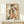 May include: Framed vintage-style Japanese geisha artwork displayed on light wood shelf against white wall. Print shows woman in elaborate floral kimono holding decorative fan, with weathered beige background and scattered dark spots. Simple wooden frame matches shelf. Small white geometric object sits nearby for scale.