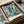 May include: Framed art print of Paul Klee's abstract composition featuring turquoise and blue tones with tropical palm fronds, geometric patterns, and golden accents, displayed in black frame inside cardboard shipping box with protective wrapping and packing materials on white surface.