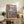 May include: Framed Japanese ukiyo-e style artwork featuring a geisha in colorful kimono seated on wooden platform with Mount Fuji and cloudy sky in background, displayed on rustic wooden console table alongside potted fern, ceramic vase, and books in warm-toned living room setting