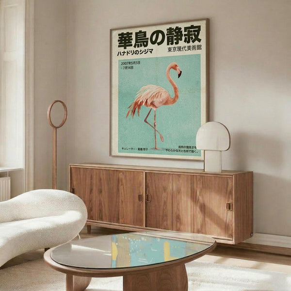May include: Japanese flamingo exhibition poster in wooden frame hanging above mid-century walnut credenza in minimalist living room. Poster features pink flamingo on turquoise background with black Japanese text. White curved chair and oval glass coffee table with abstract art visible. Brass floor lamp and table lamp provide warm lighting against neutral walls.