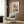 May include: Framed art poster featuring colorful abstract floral design with geometric flowers in red, yellow, blue, and pink tones displayed on wood-paneled wall above beige upholstered armchair with patterned throw pillow, brass floor lamp, and round side table with open book in modern living room setting