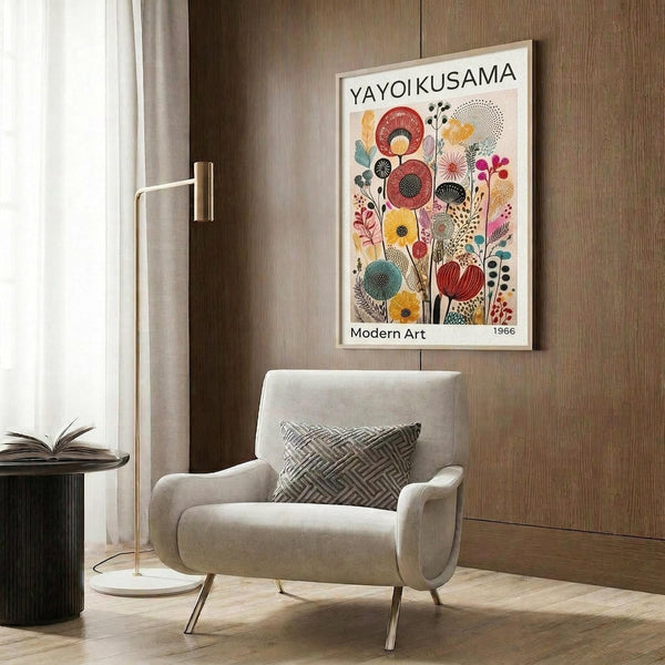 May include: Framed art poster featuring colorful abstract floral design with geometric flowers in red, yellow, blue, and pink tones displayed on wood-paneled wall above beige upholstered armchair with patterned throw pillow, brass floor lamp, and round side table with open book in modern living room setting