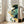 May include: Large framed poster with flowing abstract design in teal, gold, and green organic shapes resembling liquid or topographical forms, displayed on light wooden floor against white walls in bright living room with beige armchair and large windows with natural light streaming in.
