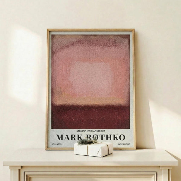 May include: Framed abstract art print in natural wood frame displaying gradient bands of deep burgundy, coral pink, and darker red tones in Rothko's color field style, displayed on light wooden console table with small wrapped gift box, against cream colored wall