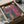 May include: Framed abstract surreal artwork in vibrant rainbow colors featuring flowing wavy lines and geometric shapes, with white Japanese characters visible in upper left. Art print shown in black frame nestled in brown cardboard shipping box with protective tissue paper padding. Colorful swirling patterns in red, orange, yellow, green, and blue create dreamlike landscape composition.