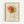 Framed art print featuring an abstract line drawing of a rose with flowing, curved black lines forming layered petals in warm orange and coral watercolor washes, along with simple line-drawn leaves on a cream background, displayed against a white wall in a natural wood frame