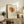May include: Framed Picasso-style line art poster featuring an abstract rose with flowing circular lines in orange and green watercolor tones, displayed on a rustic wooden sideboard alongside leather sofa, potted fern, ceramic vases, and stacked books in a warm-toned living room setting.