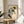 May include: Framed reproduction of early 20th century expressionist artwork showing a seated woman with curly brown hair wearing a green blouse and dark stockings, displayed on a round wooden side table next to a beige upholstered chair with plant leaves visible in soft natural lighting