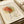 Minimalist line drawing poster of a rose in Picasso's style, featuring continuous black lines forming the flower and stem with orange and yellow watercolor washes. The cream-colored print shows "PICASSO" at top and "Centre Pompidou" at bottom, with artist signature visible. Limited edition numbering "04/150" appears in corner. The framed artwork lies on white fabric alongside rolled paper tubes, creating an elegant flat lay composition.