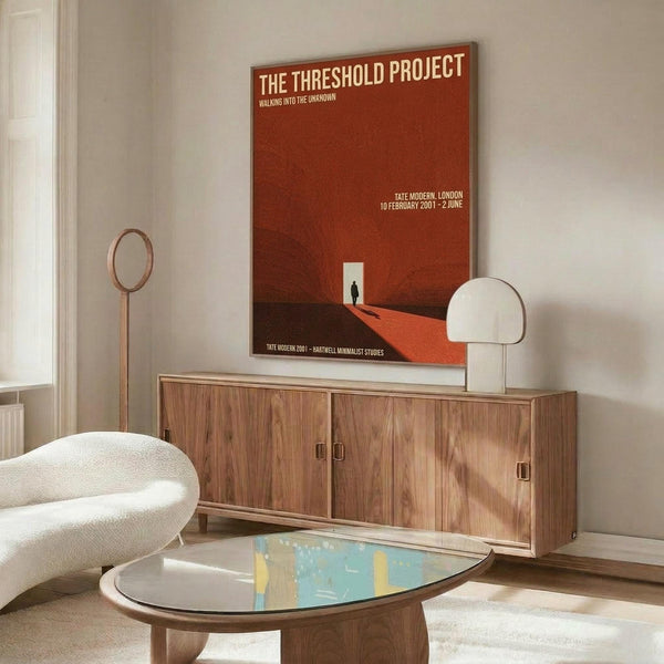 May include: Red vintage exhibition poster hanging above wooden sideboard in modern living room. Poster features minimalist design with silhouette figure in white doorway against burnt orange background. Room styled with cream curved chair, glass coffee table, white table lamp, and brass floor mirror. Clean Scandinavian aesthetic with natural wood tones and neutral walls.