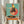 May include: Person in cream ruffled sleeves holding framed artwork showing a stylized rooster wearing sunglasses and polka dot outfit, dancing on a vintage turntable against turquoise background with coral circle. Dried pampas grass visible to left, neutral interior setting with white curtains.
