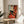 May include: Framed reproduction of Modigliani's painting featuring a woman with auburn hair in a black dress sitting on a red chair. The artwork shows the artist's characteristic elongated style with muted earth tones. Displayed on a round wooden side table next to a beige upholstered chair in a sunlit room with white walls and plant shadows.
