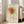 May include: Framed poster featuring a minimalist line drawing of a rose in Picasso's style, with orange and green watercolor washes on cream background, displayed on wooden floor next to beige sofa near bright windows in modern living room setting