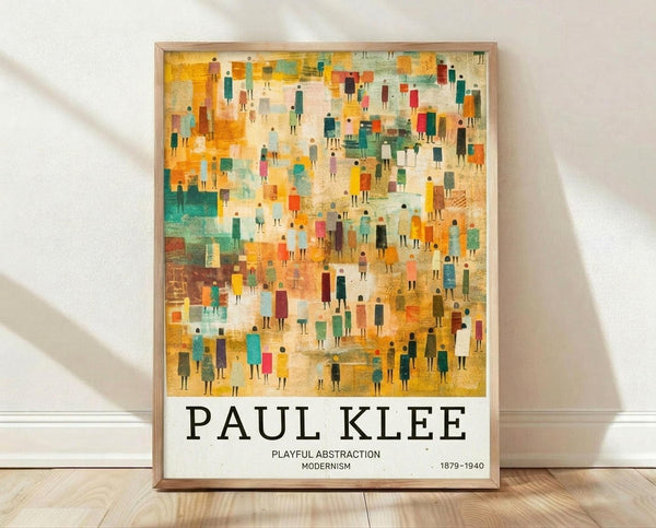 May include: Framed poster with abstract modernist artwork featuring hundreds of small colorful human figures in geometric shapes scattered across a warm golden, orange, and teal background. The print displays "PAUL KLEE" in large black text below the artwork, with "PLAYFUL ABSTRACTION MODERNISM 1879-1940" in smaller text. Light wood frame leans against white wall on natural wood flooring with soft shadows.