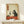 May include: Framed poster print displayed on light wood console table against white wall. Artwork shows black cat in Japanese ukiyo-e style holding wine glass, sitting at red-orange table with wine bottle, grapes, and cheese. Features aged beige background with Japanese text in red cartouche. Natural wood frame matches console. Small white gift box with greenery sits beside frame.