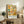 May include: Colorful abstract art poster with geometric figures in yellows, oranges, teals and earth tones, displayed in thin wooden frame on rustic wood sideboard. Room styled with fern plant, beige chair, ceramic vases and books creating warm, modern living space with white walls.
