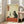 May include: Framed poster print displayed in bright living room with beige sofa and large windows. Artwork shows Japanese-style illustration of black cat holding wine glass at red table with wine bottle, grapes, and cheese. Features vintage cream background with orange text banner in upper left corner. White wooden frame leans against white wall on hardwood floor.