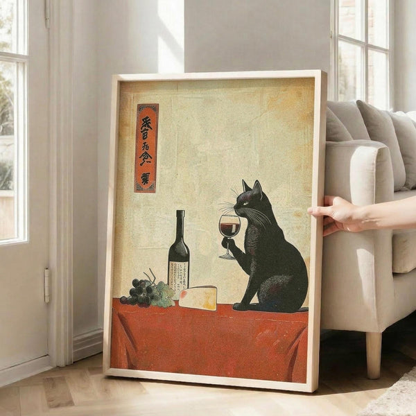 May include: Framed poster print displayed in bright living room with beige sofa and large windows. Artwork shows Japanese-style illustration of black cat holding wine glass at red table with wine bottle, grapes, and cheese. Features vintage cream background with orange text banner in upper left corner. White wooden frame leans against white wall on hardwood floor.