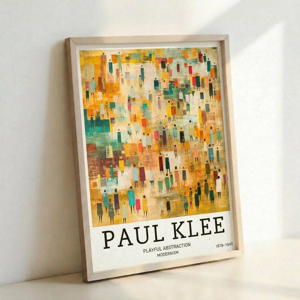 May include: Framed art print leaning against white wall showing abstract modernist artwork with hundreds of small colorful human figures in warm yellows, oranges, teals and earth tones. Light wood frame contains poster with "PAUL KLEE" and "PLAYFUL ABSTRACTION MODERNISM 1879-1940" text at bottom. Textured, painterly style with geometric and organic shapes creating crowd-like composition.