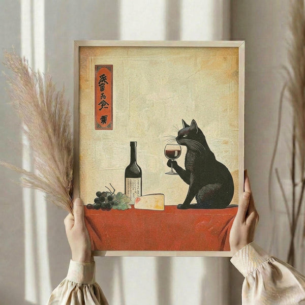 May include: Person holding framed artwork in cream-colored room with dried wheat stalks. Print shows black cat in Japanese ukiyo-e style holding wine glass, sitting at red table with wine bottle, grapes, and cheese on aged parchment background. Features Japanese text in red banner. Light wood frame, neutral wall backdrop.