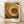 May include: Framed art print featuring concentric circles of dots in warm earth tones - yellows, oranges, browns, and black - creating a hypnotic spiral pattern. Text reads "YAYOI KUSAMA" and Japanese characters with "TOKYO" below. Light wood frame sits on wooden floor against white textured wall with soft natural lighting casting shadows.