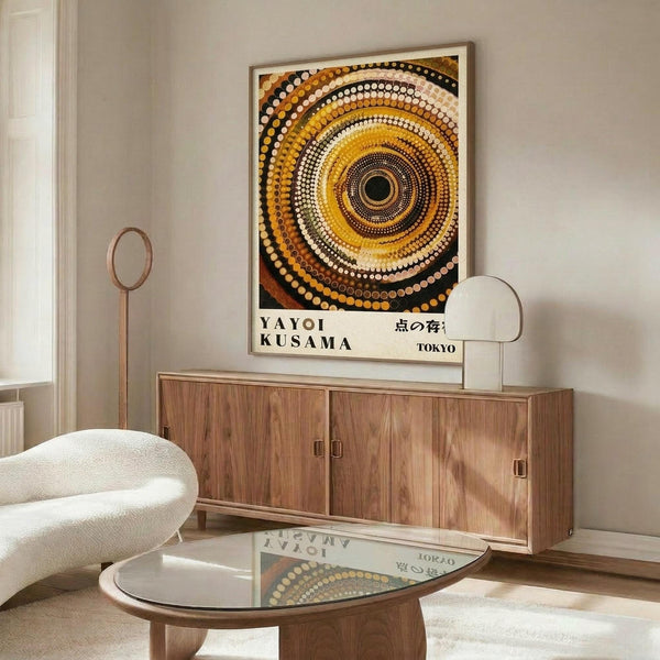 May include: Framed poster with concentric circles in warm earth tones - yellows, oranges, browns, and white dots radiating from black center, displayed above wooden sideboard in modern living room with cream chair, glass coffee table, and floor lamp
