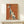 May include: Framed poster print featuring an elegant greyhound illustration in teal and cream colors against a warm terracotta orange background, displayed on a light wood shelf against a white wall. The vintage-style artwork shows the slender dog in profile with French text reading "L'élégance ne vieillit pas de noir et d'or" in golden lettering. The print has a natural wood frame and textured paper appearance.
