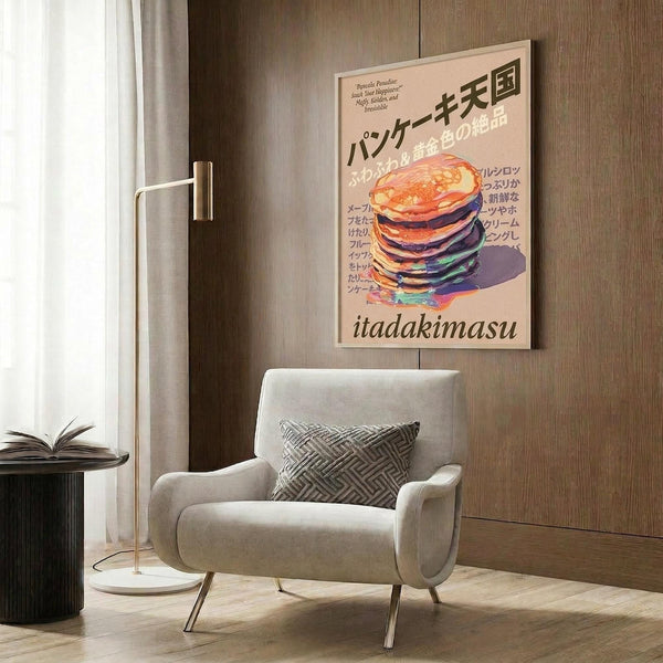 May include: Framed poster featuring colorful illustrated stack of pancakes with Japanese text and "itadakimasu" at bottom, displayed on wood-paneled wall above beige upholstered armchair with geometric patterned pillow. Modern brass floor lamp and dark round side table with open book complete the warm, contemporary living room setting with natural lighting from nearby window.