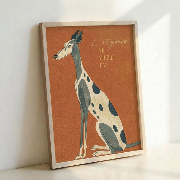 A stylized illustration of a sitting greyhound with dark gray and cream spotted markings on a warm orange textured background. The elegant dog sits upright in profile with French text reading "L'élégance ne vieillit pas" in golden lettering. The artwork is displayed in a light wooden frame leaning against a white wall, creating soft shadows on the surface below.