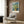 May include: Van Gogh poster print showing yellow flowers in a vase against blue brushstrokes, hung on wood paneled wall above beige upholstered chair with geometric pillow. Modern floor lamp and side table with open book complete the neutral-toned reading nook setting.