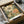 May include: Vintage botanical art print in black frame inside cardboard shipping box with protective tissue paper. Artwork features large detailed flowers in cream, pink and orange tones with green leaves on olive background with dotted patterns. Print shows artist signature and appears to be museum-quality reproduction with warm, earthy color palette.