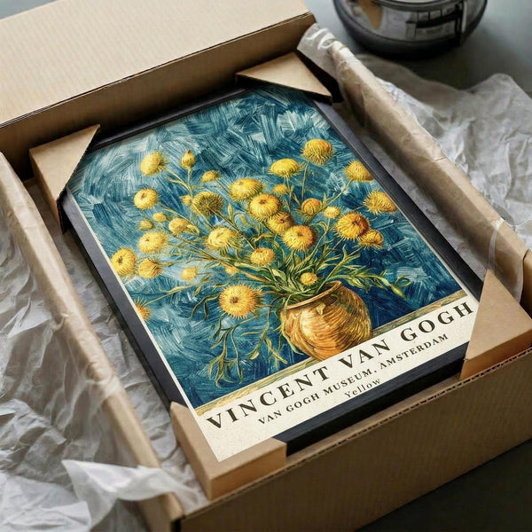 May include: Van Gogh print in black frame being unboxed from brown cardboard packaging with white tissue paper. The artwork shows yellow chrysanthemum flowers in a brown vase against swirling blue background. Print has white border with "VINCENT VAN GOGH" and "VAN GOGH MUSEUM, AMSTERDAM" text at bottom. Wooden dowels visible as protective packaging elements.