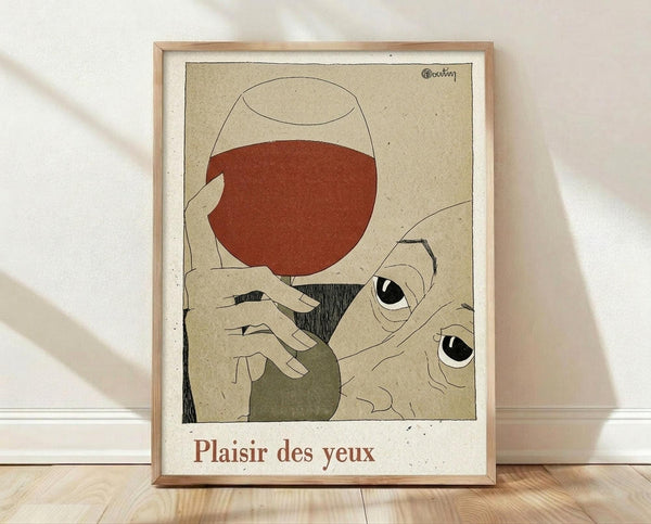 May include: Framed art print leaning against white wall on light wood floor. The poster features a minimalist illustration of hands holding a wine glass filled with red wine, with two large eyes peering from below. The artwork uses muted earth tones - beige, rust red, olive green, and black line work on textured paper background. French text "Plaisir des yeux" appears at bottom in red lettering. Natural wood frame surrounds the print.